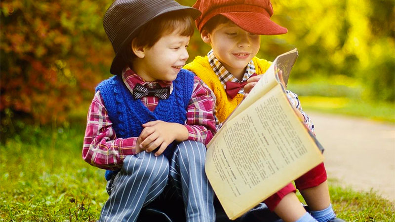 Two young boys sitting outside reading a book