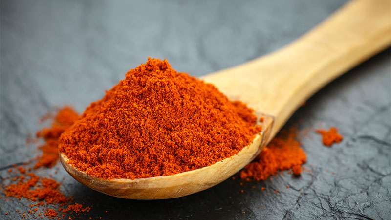 Photo of ground paprika heaping in the bowl of a wooden spoon.
