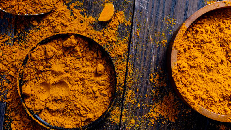 Photo of ground turmeric in a couple of wooden bowls on a wooden table.